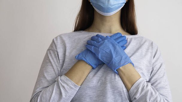 Жінка з хірургічною маскою тримає руки в латексній рукавичці на серці
. - Фото, зображення