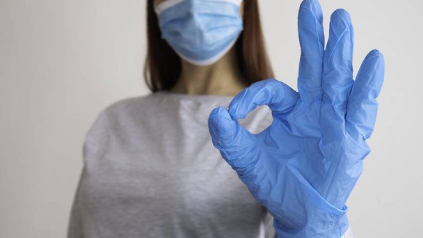 Vrouw met een chirurgisch masker toont met de handen in latex handschoen een symbool OK. - Foto, afbeelding