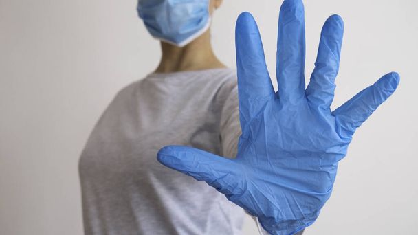 Femme avec un masque médical et les mains en gant de latex montre le symbole ARRÊT. Arrêtez la maladie.
. - Photo, image