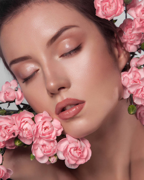 close-up beauty portrait of young beautiful woman. natural and dewy make-up look. spring concept. caucasian lady with closed eyes. pink flowers near her face. natural beauty concept. glowing skin - Φωτογραφία, εικόνα