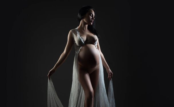 Belly of a pregnant woman. Pregnancy. Woman studio intimate portrait. Happy pregnant woman. Happy pregnant. Isolated on black studio background. - Fotó, kép