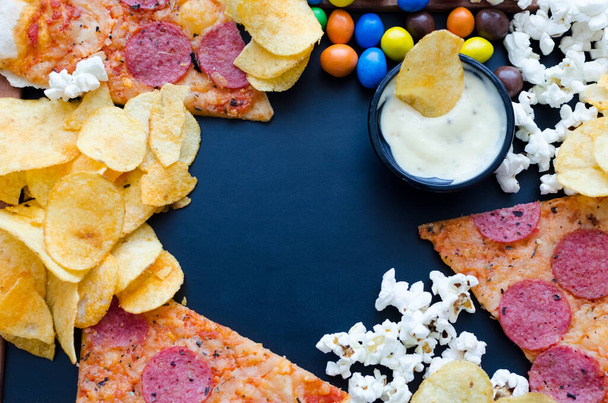 Fast food en ongezond eten concept. Sluiten van fastfood snacks: pizza, popcorn, chips en snoepjes. Assortiment van koolhydraten producten slecht voor figuur en tanden. Bovenaanzicht. Kopieerruimte. - Foto, afbeelding