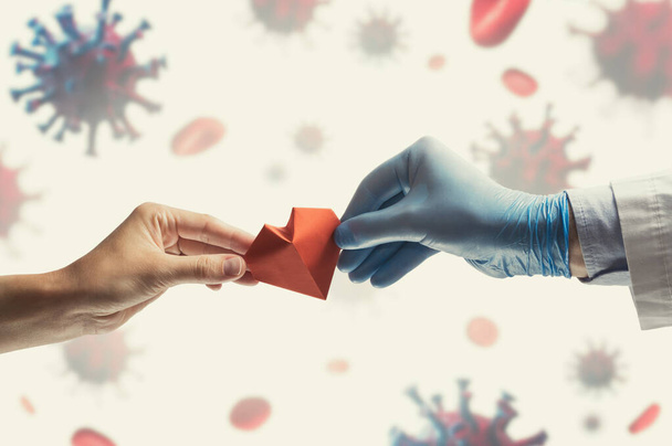 Az orvos keze piros papírszívet ad egy nőnek. Kép a háttérben a coronavirus covid-19-cel. Az orvosi kezelés koncepciója a kovid-19 világjárvány idején - Fotó, kép