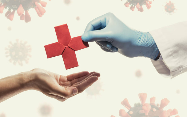 Lääkärin käsi antaa naiselle punaisen paperiristin. Kuva taustalla sepelvaltimovirus covid-19. Lääketieteellisen hoidon käsite pandemian aikana covid-19
 - Valokuva, kuva