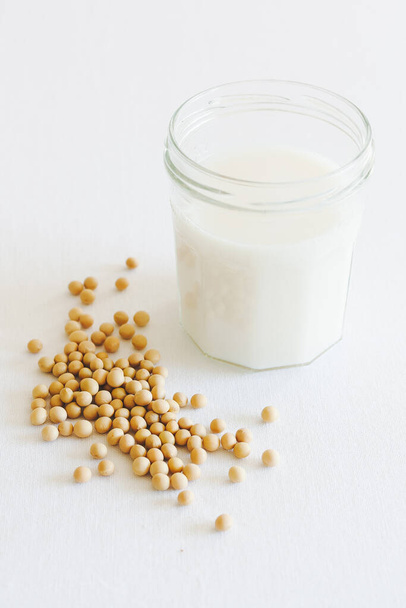 Un bicchiere di latte di soia fatto in casa a base vegetale con fagioli di soia come decorazione in formato verticale con sfondo bianco
. - Foto, immagini