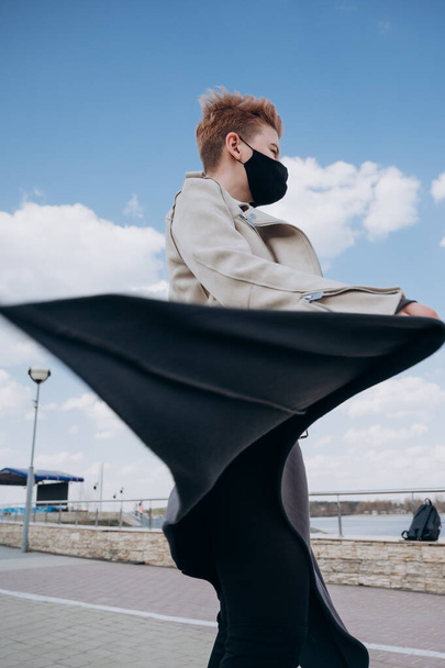 a girl with short hair walks down the street in a black antiviral mask - Foto, afbeelding