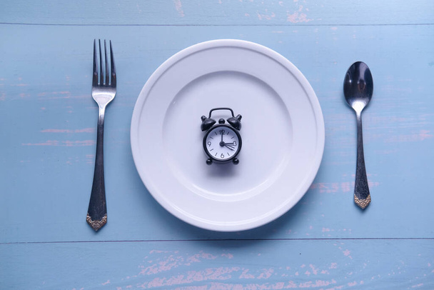 Alarm clock with fork, knife and plate on the table. Top view. Time to eat - Zdjęcie, obraz