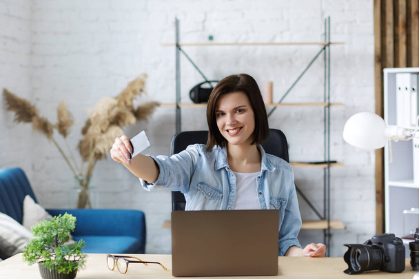 Young freelancer in home office holding credit card and using laptop. Online shopping, online payments. Booking tickets online. Modern technologies concept - Photo, image