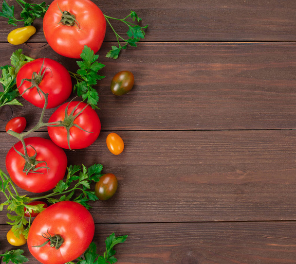 Κόκκινες ντομάτες και ντοματίνια διαφόρων χρωμάτων με φύλλα μαϊντανού σε ρουστίκ ξύλινο τραπέζι με χώρο για κείμενο. Νωπά λαχανικά για υγιεινή διατροφή - Φωτογραφία, εικόνα