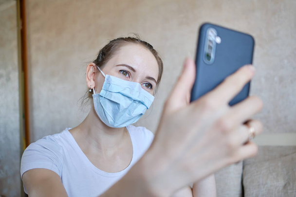 La fille dans un masque médical est sur l'auto-isolement à la maison et communique par chat vidéo via smartphone. Gros plan
. - Photo, image