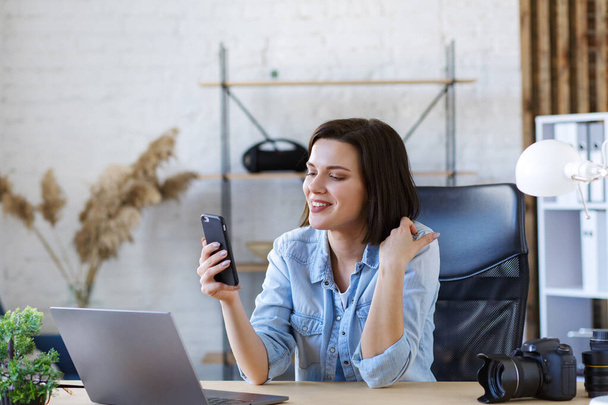 Working from home.Communication online with colleagues and freelancers.Portrait of young woman using smartphone and smiling.Mobile phone apps, texting message,browsing internet, looking at smartphone - Foto, imagen