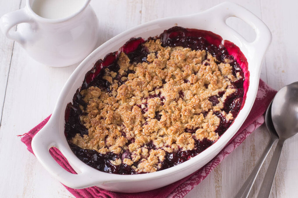 Berry crumble in white baking dish on white wooden background. - Photo, Image