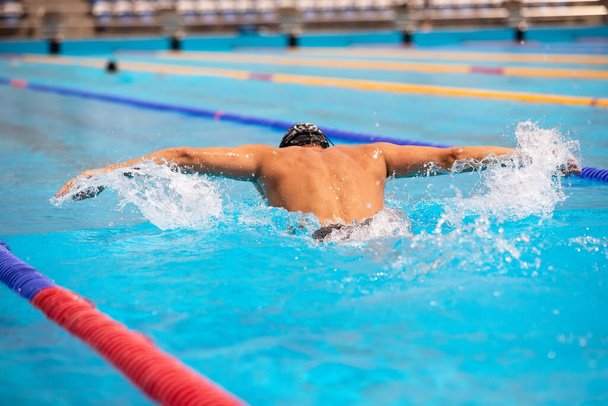 Athletic man swimming in butterfly style in the swimming pool with clear blue water. - Photo, image
