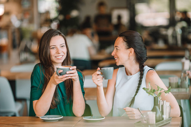 Ευτυχισμένες χαμογελαστές νεαρές γυναίκες με φλιτζάνια καφέ στο καφέ. - Φωτογραφία, εικόνα