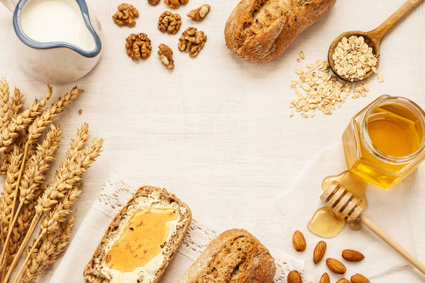 Rural or country breakfast - bread rolls, honey jar, milk, nuts and wheat on white wood from above. Background layout with free text space. - Foto, imagen
