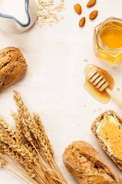 Rural or country breakfast - bread rolls, honey jar, milk, nuts and wheat on white wood from above. Background layout with free text space. - Foto, imagen