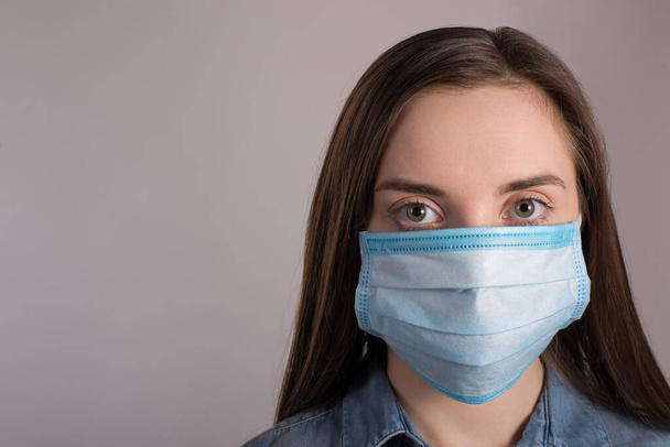 Coronavirus outbreak concept. Close up photo of woman wearing facial medical mask protecting against pandemic isolated over grey background with copy empty space - Zdjęcie, obraz