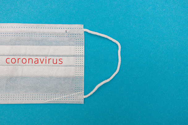 Medisch wegwerp gezichtsmasker op een blauwe achtergrond met de inscriptie stop coronavirus covid 19. Wereldpandemie coronavirus. Stop de pandemie. Gezondheid en preventie van influenza en een besmettelijke ziekte - Foto, afbeelding