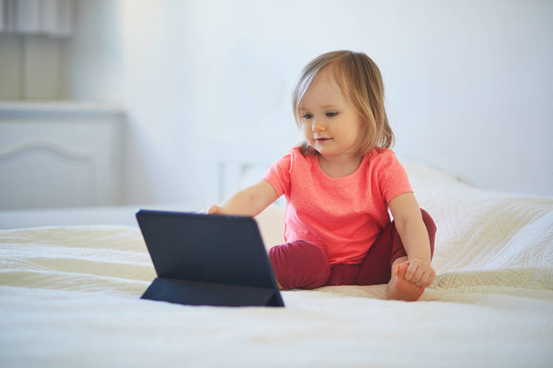 Evde dijital tableti olan küçük bir kız. Çocuk çizgi film izliyor. Çocuk arkadaşlarıyla ya da anaokulu öğrencileriyle iletişim kurmak için alet kullanıyor. Çocuklar için eğitim ve uzak mesafe eğitimi. Evde kalıp eğlenin. - Fotoğraf, Görsel