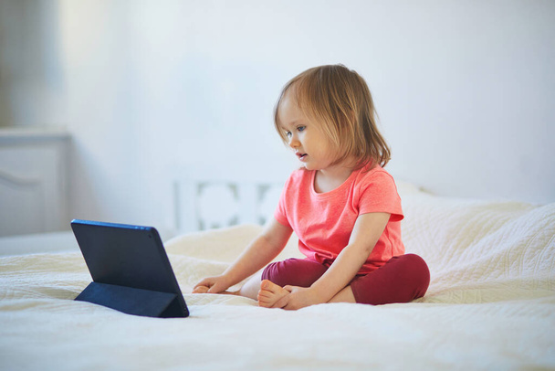 Toddler girl with digital tablet at home. Child watching cartoons. Kid using gadget to communicate with friends or kindergartners. Education and distance learning for kids. Stay at home entertainment - Foto, immagini