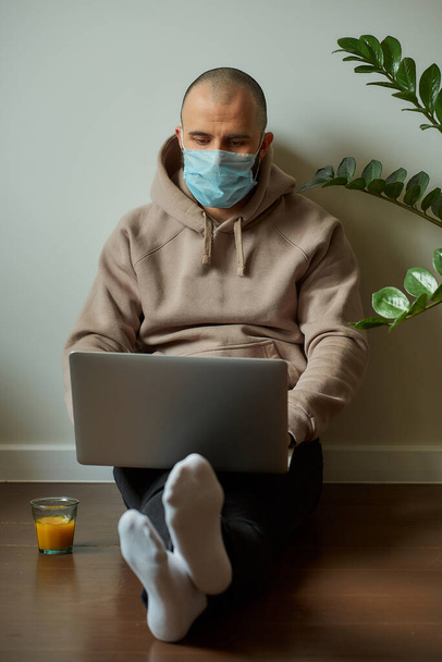 Travail à distance. Un homme dans un masque médical pour éviter la propagation du coronavirus travaillant à distance sur son ordinateur portable pendant la quarantaine. Un programmeur chauve travaillant à domicile pendant la pandémie de COVID-19
. - Photo, image