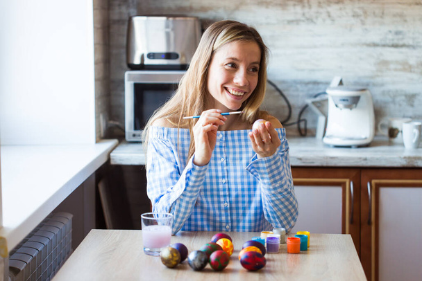 Holidays, handmade and creation concept - Happy young woman draws on Easter egg. - Photo, Image