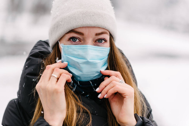 Uma menina em uma máscara médica estéril protege contra o vírus da gripe ao ar livre em um dia nevado molhado e molhado
 - Foto, Imagem