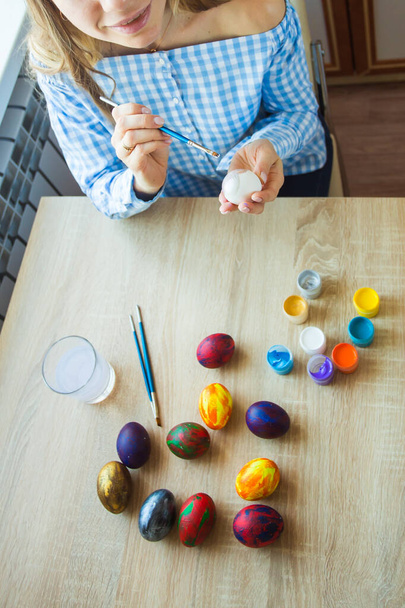 Ünnepek, kézműves és teremtés koncepció - Boldog fiatal nő merít húsvéti tojás, közelkép. - Fotó, kép