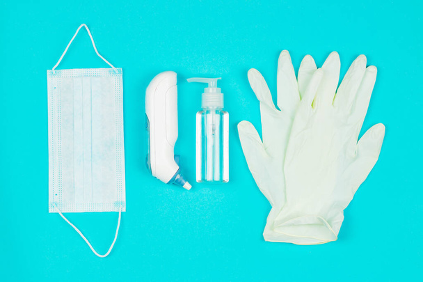 Медицинская маска, термометр, белые латексные перчатки и гель для дезинфекции рук на синем фоне
. - Фото, изображение