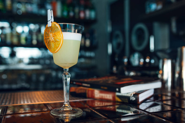 Pisco Sour cocktail with dried orange slice at bar or restaurant background. Closeup. - 写真・画像