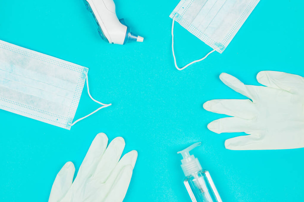 Medische masker, thermometer, witte latex handschoenen en hand ontsmettingsgel op blauwe achtergrond. - Foto, afbeelding