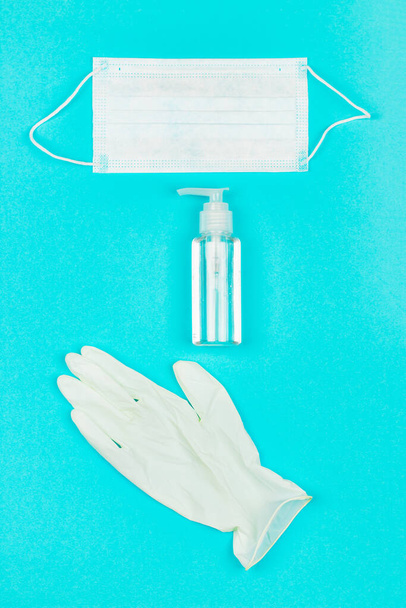 Ιατρική μάσκα, λευκά γάντια λάτεξ και τζελ καθαρισμού χεριών σε μπλε φόντο. - Φωτογραφία, εικόνα
