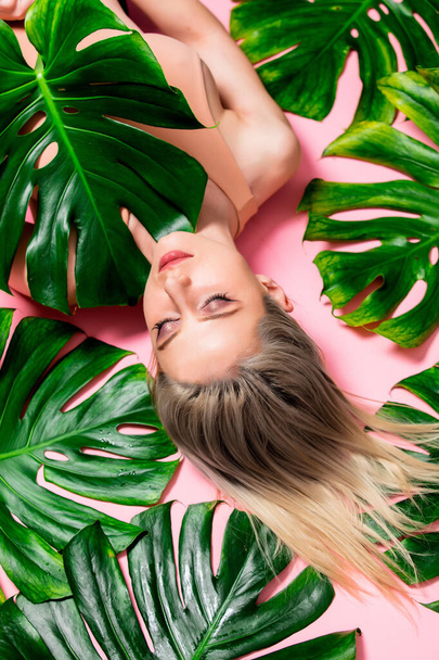 Beautiful blonde woman with palm leaves lying on pink background  - Fotografie, Obrázek