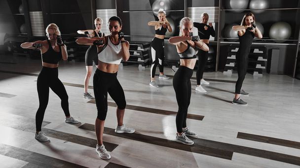 Women in black and white sportswear on a real group body Combat workout in the gym train to fight, kickboxing with a trainer - Foto, Imagem