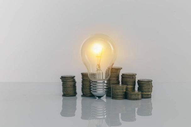 Ruka drží žárovku s hromadou mincí. Tvůrčí nápady na úsporu peněz. Správa peněz do budoucna - Fotografie, Obrázek