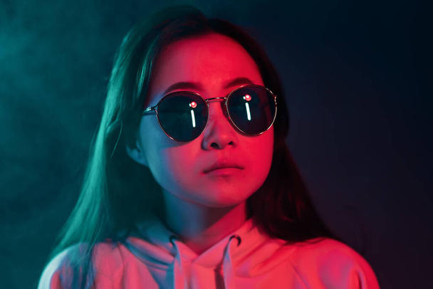 Millennial pretty asian girl with long hairstyle with neon light. Mysterious hipster teenager in glasses. - Φωτογραφία, εικόνα
