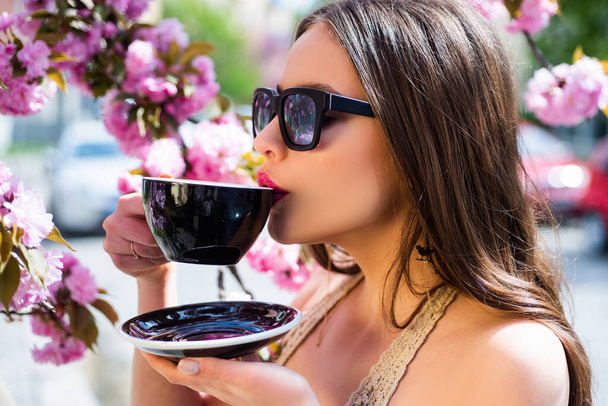 Close up portrait of beautiful girl hold cup of cofee with matcha. Good morning. Warm spring flower background. Trendy drink latte matcha or mocha. - Фото, зображення