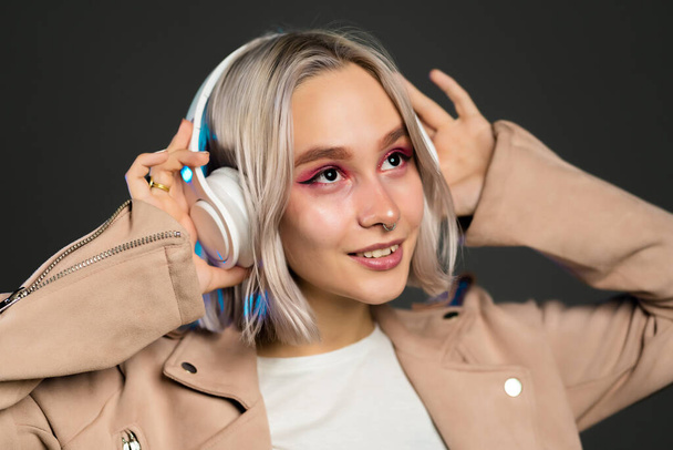 Mysterious hipster teenager listening to music with headphones. Portrait of millennial pretty girl with short hairstyle on grey background. Dyed hair. - Foto, Imagem