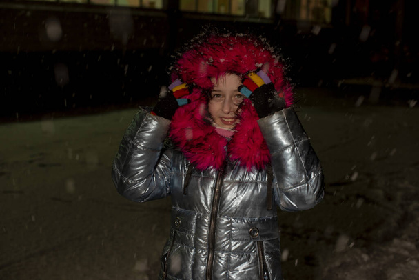 retrato de una hermosa niña de nueve años. Niña de 9 años con chaqueta azul. Niño de escuela en invierno. Adolescente. Invierno y nieve. Noche nevada. El niño disfruta de la nieve. Chaqueta con piel ecológica
 - Foto, imagen
