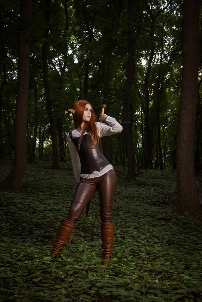 Elfí žena v kožené zbroji s mečem na pozadí lesa. Cosplay. - Fotografie, Obrázek