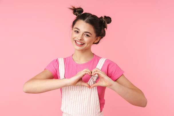 Photo of lovely charming girl smiling and showing heart with fingers isolated over pink background - Fotó, kép