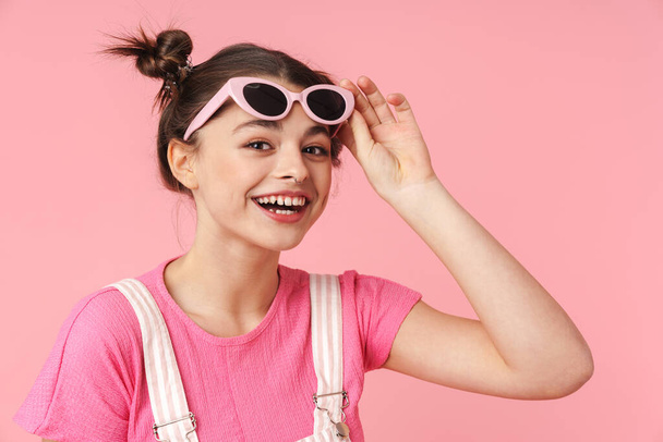 Фото радісної чарівної дівчини в сонцезахисних окулярах позує і сміється ізольовано на рожевому фоні
 - Фото, зображення