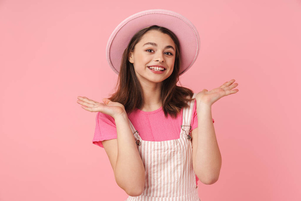Photo of lovely charming girl in hat smiling and looking at camera isolated over pink background - Fotó, kép