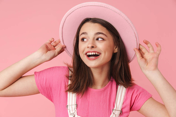 Photo of lovely charming girl in hat smiling and posing at camera isolated over pink background - Foto, Bild