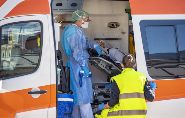 Alarm-Pandemie Covid-19. Ärzte mit Schutzmasken helfen einem Mann mit Coronavirus, der in einem Rettungswagen auf einer Trage liegt. Weltweiter Warnalarm. Transportlogistik für den Notfall - Foto, Bild