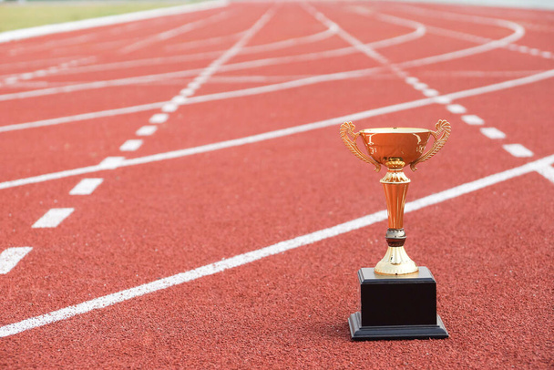 Un trofeo de oro en pista de atletismo / Concepto de competición por el éxito
 - Foto, Imagen