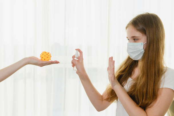 Молода жінка в медичній масці використовує спрей-антисептик на іграшці жовтого каучуку для гри під час ізоляції вдома, захист під час епідемічного коронавірусу. Іграшка схожа на вірус
. - Фото, зображення