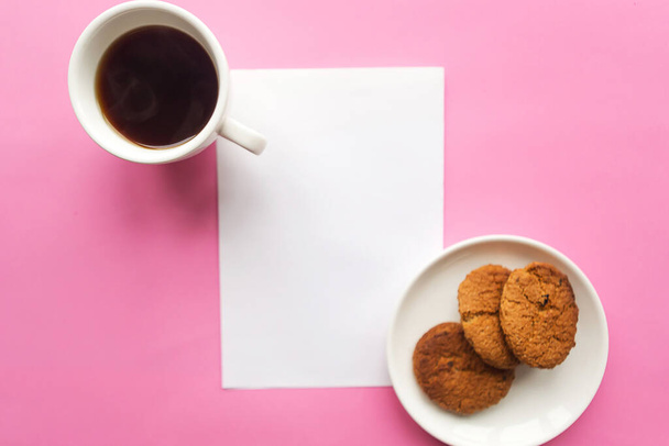 Flat lay photo with coffee cup, raisins cookies and white mockup blank on pink background. Freelance concept - Φωτογραφία, εικόνα