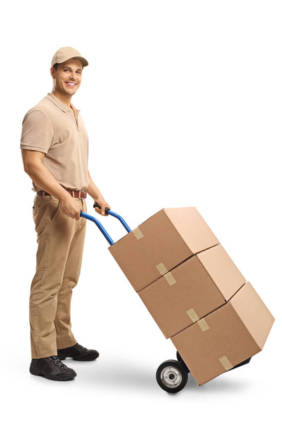 Full length shot of a delivery man pushing a hand truck with boxes isolated on white background - Photo, image