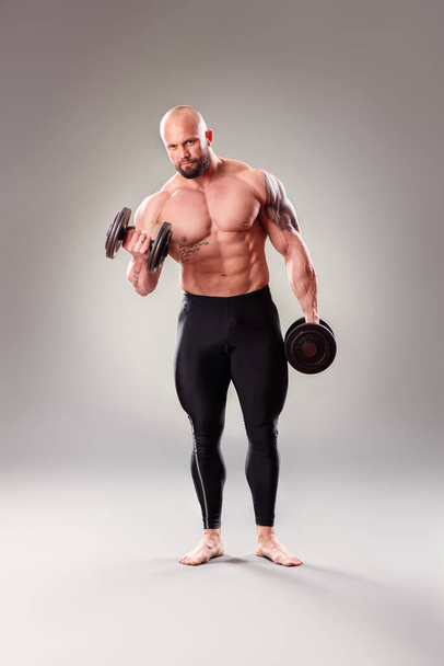 Sexy muscular bodybuider posing with weights on the gray background - Foto, Imagen